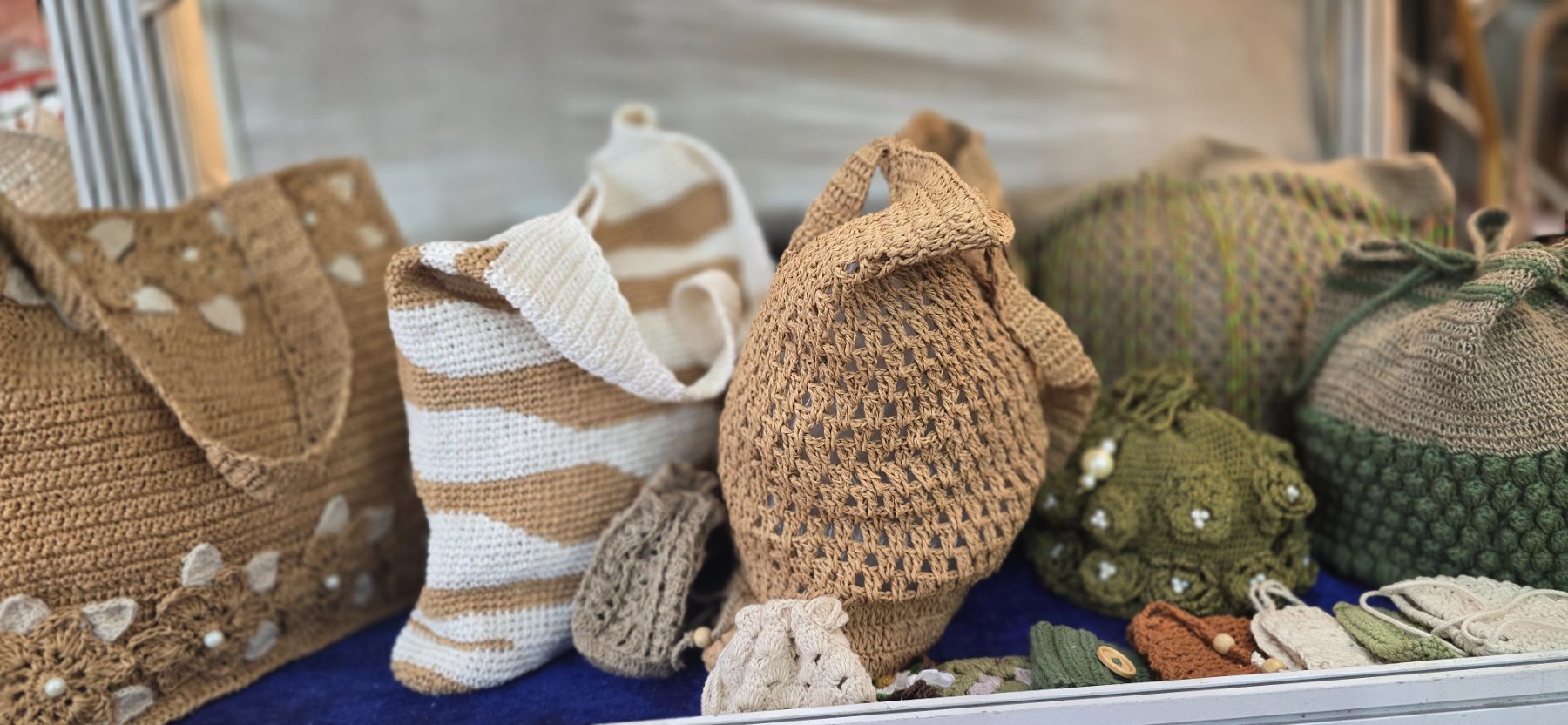 Crochet bags in natural, cream and olive yarns on display.