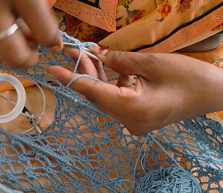 Hands working a blue crochet net with a hook.