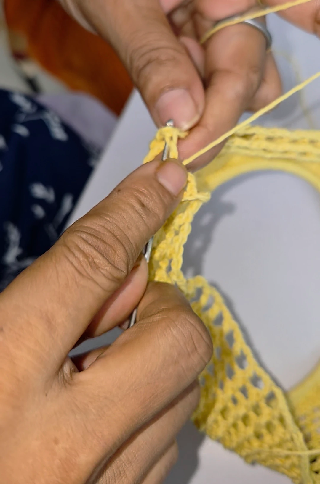 Hands shaping a yellow crochet round with a hook.