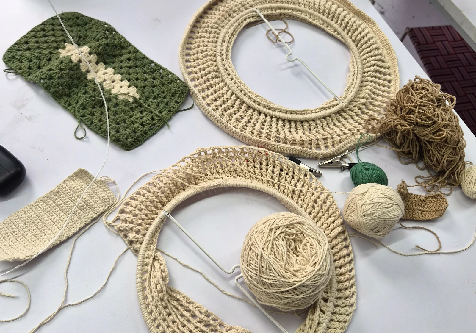 Crochet rings in progress, a green panel and balls of cotton yarn on a worktable.