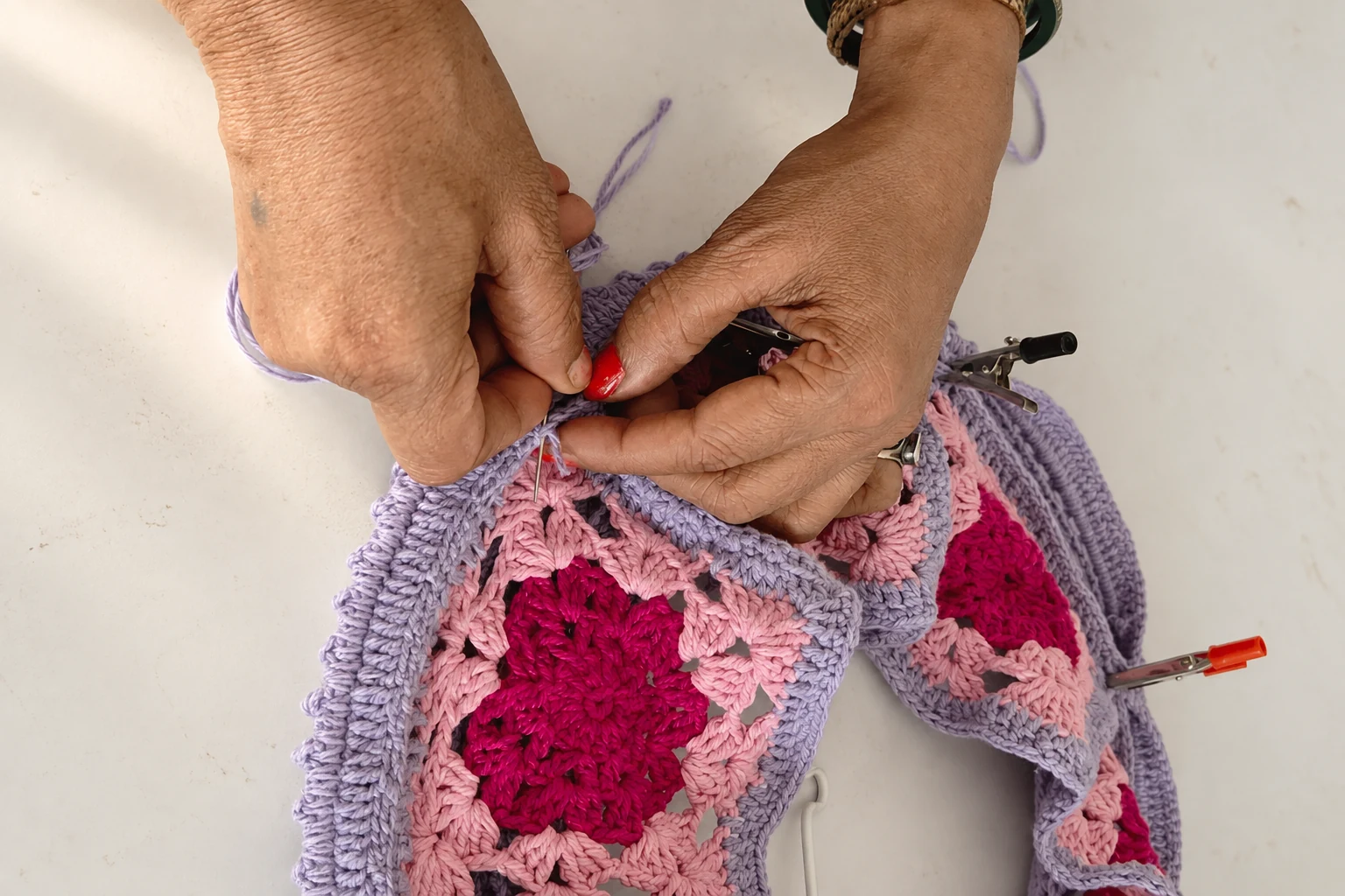 Artisan hands crocheting pink and lilac floral textile panels.