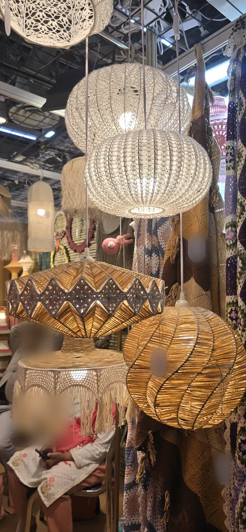 Raffia and crochet pendant lamps glowing amber above a fringed lampshade, at our stall, IHGF Delhi Fair Spring 2026.
