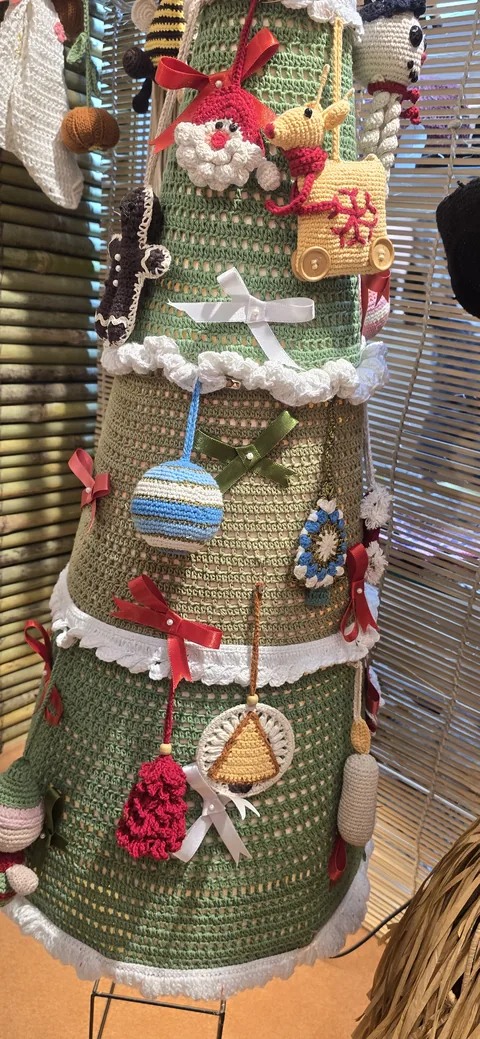 A tall green crochet Christmas tree hung with crochet baubles, bells, red bows and small figures, at our stall, IHGF Delhi Fair Spring 2026.