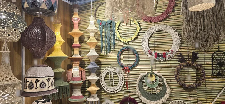 A long wall at our stall, IHGF Delhi Fair Spring 2026: crochet pendant lamps and tall stacked lamps beside rows of crochet and macramé wreaths and wall hangings.