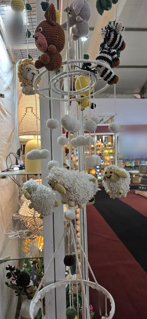 A crochet nursery mobile of animals, among them a lion, an elephant, a zebra and three sheep, with crochet clouds, hanging at our stall, IHGF Delhi Fair Autumn 2025.