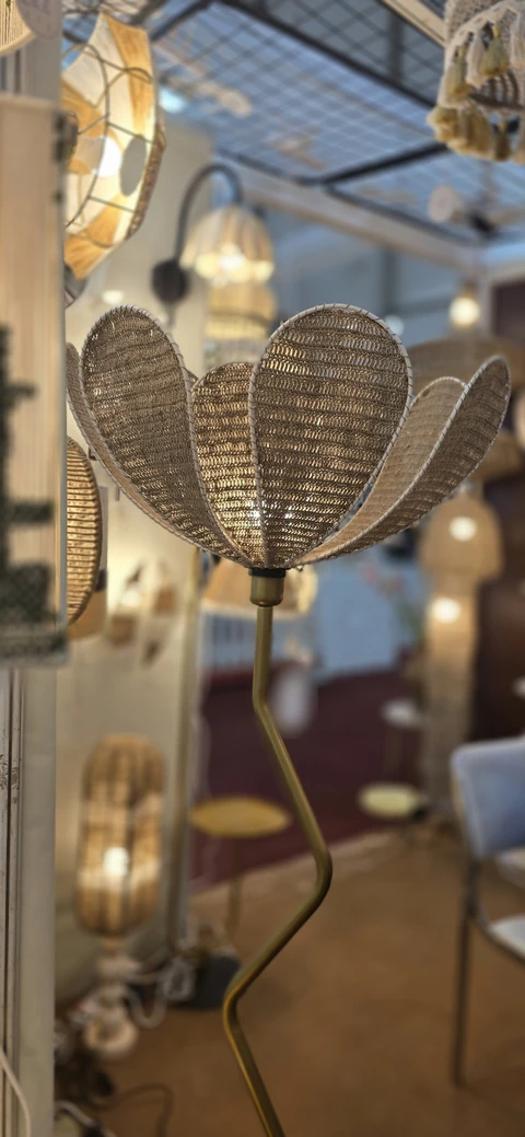 A floor lamp with a woven petal shade on a curved brass stem, lit among pendant lamps at our stall, IHGF Delhi Fair Autumn 2025.