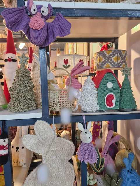 Shelves of crochet pieces at our stall, IHGF Delhi Fair Autumn 2026: a purple bat, Santa figures, Christmas trees, a green and red house, a basket and cream and pink bunnies.