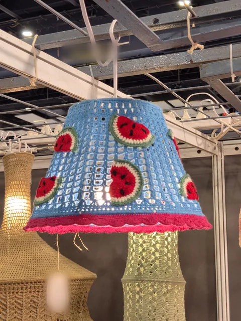 A blue crochet lampshade with red watermelon slices and a pink scalloped edge, lit at our stall, Bharatiya Vyapar Mahotsav 2026.