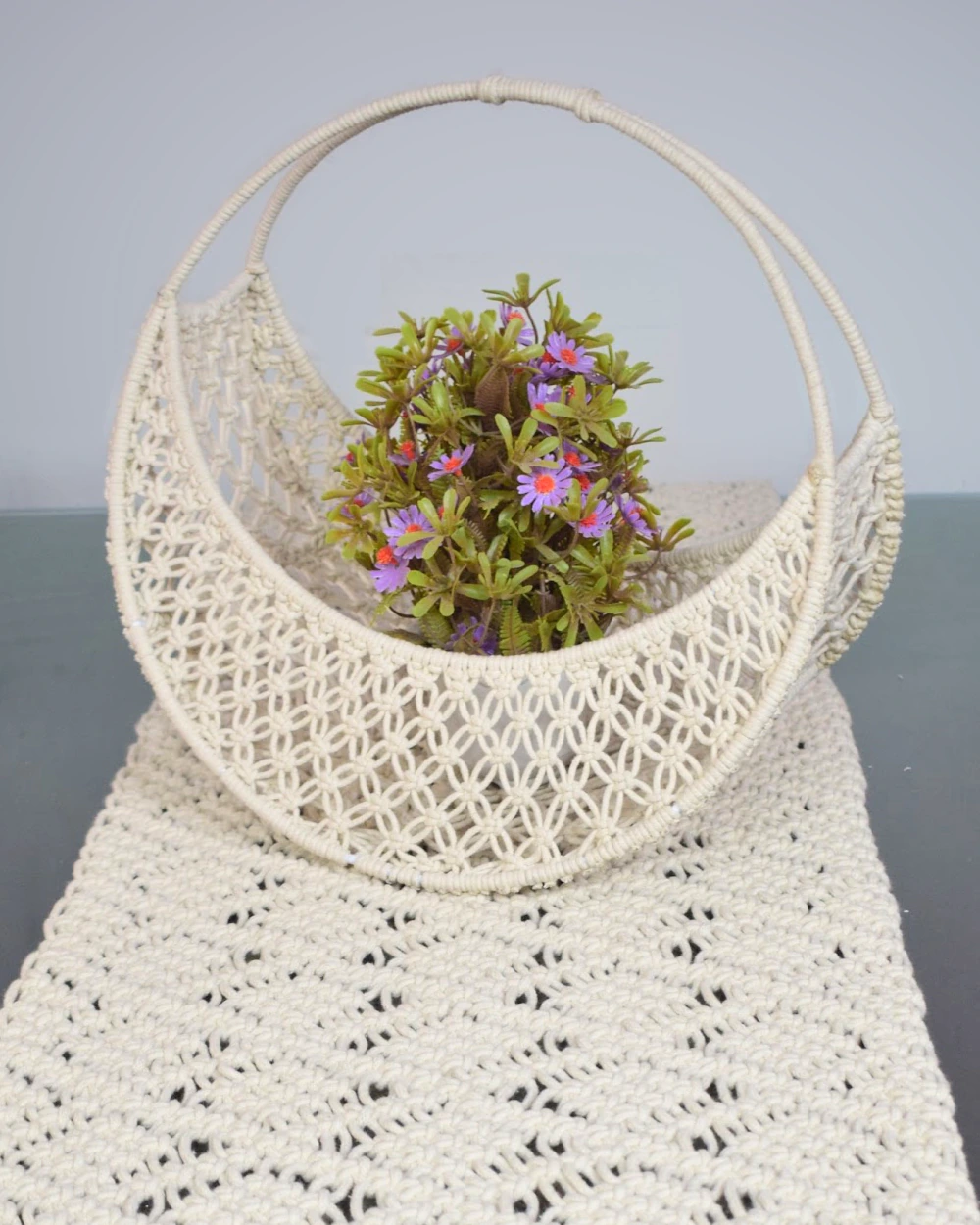Cream openwork basket with an arched handle, styled with flowers on a table runner.
